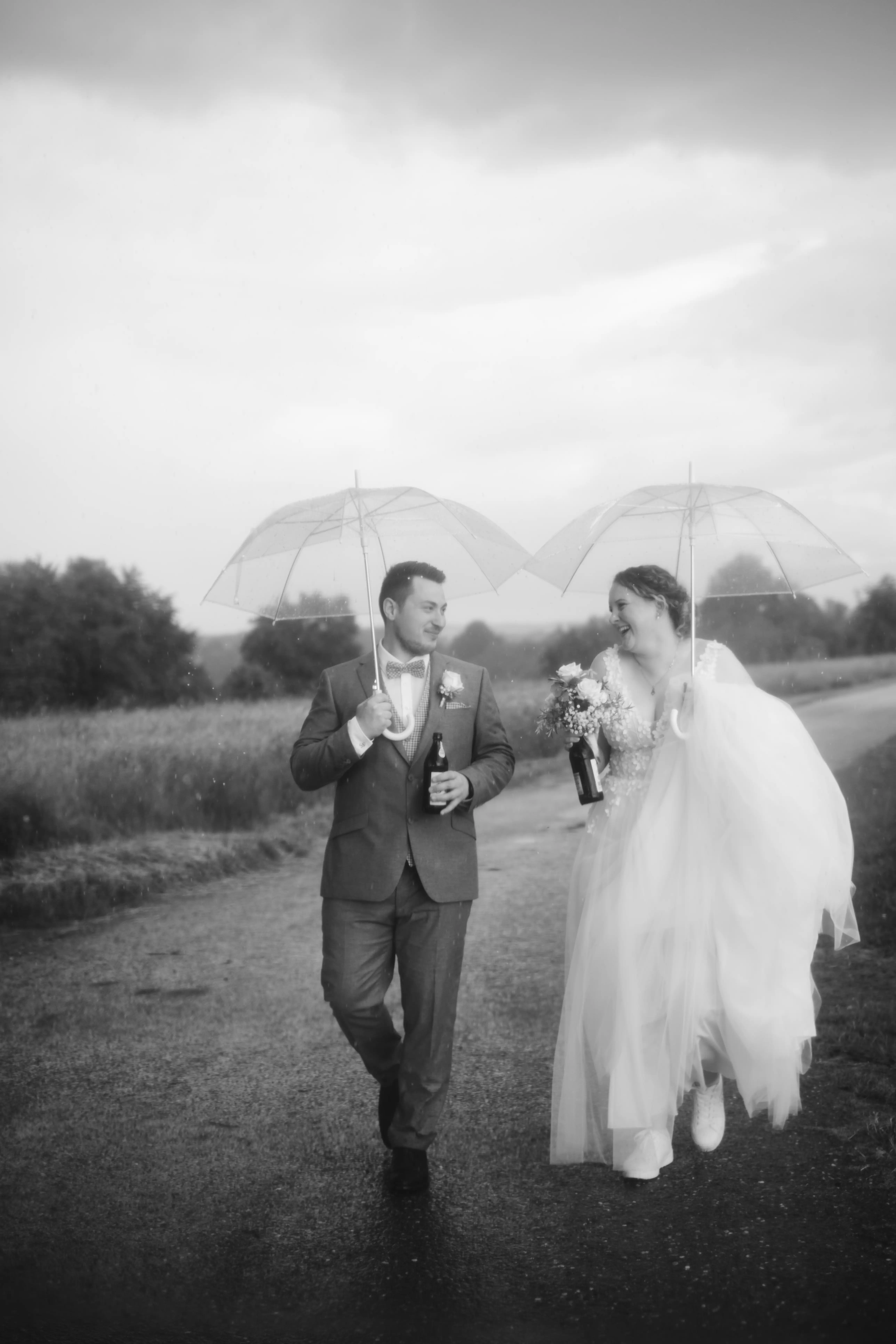 Hochzeitspaar mit Regenschirmen und einem Bier in der Hand